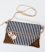 Image of a foldover clutch in navy + white stripe with a removable strap!